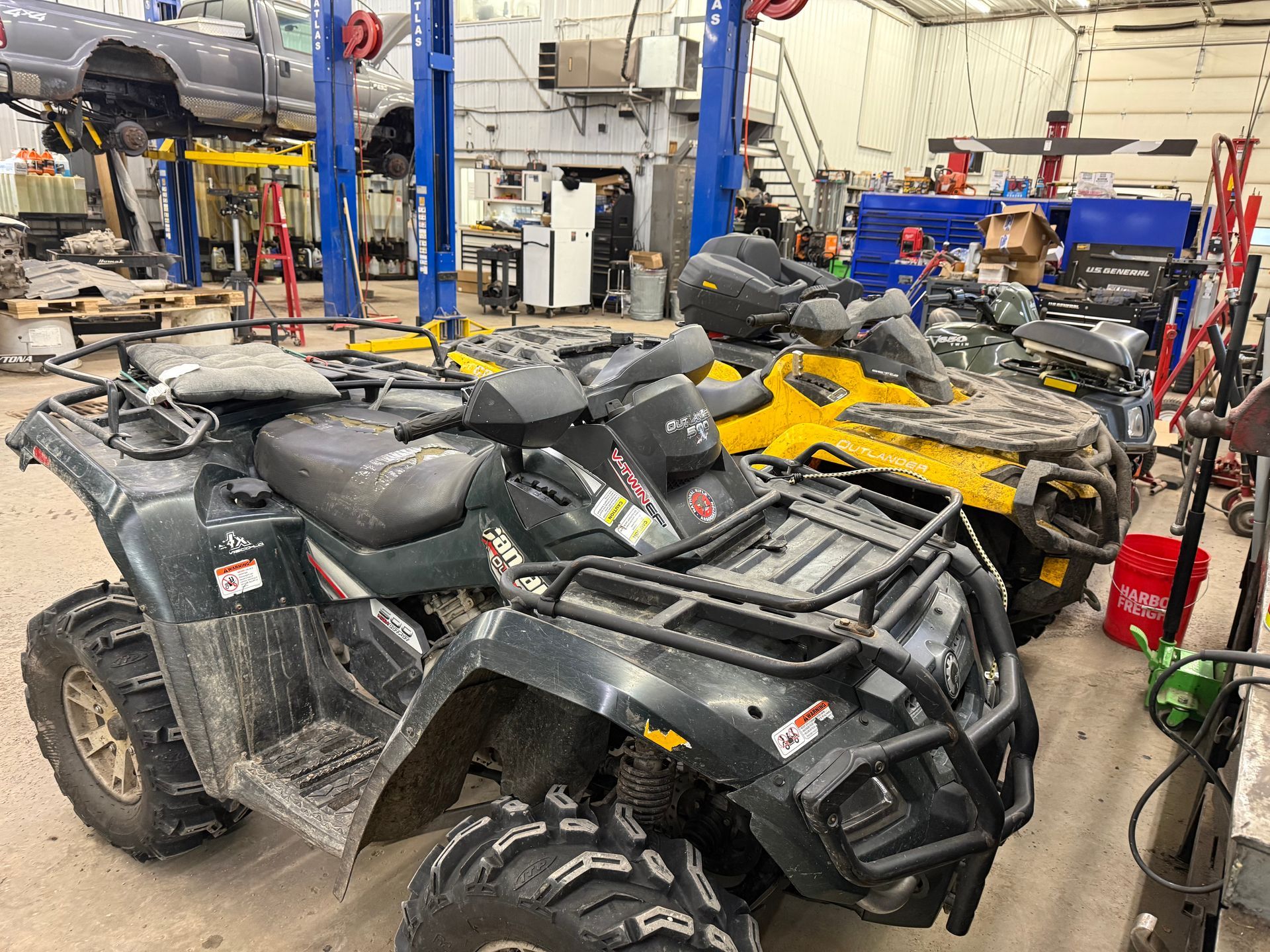 Black and yellow ATVs in a repair shop with tools and vehicle lifts around them | Itasca Automotive 
