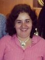 A woman in a pink shirt is sitting at a table with wine glasses.