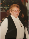 A woman wearing glasses and a black vest is standing in front of a christmas tree.