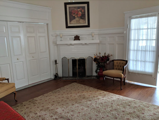 Living room with fireplace, white paneling, wooden floors, floral rug, and two chairs.