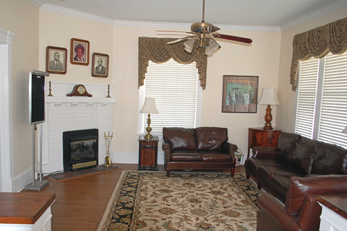 Living room with fireplace, two leather sofas, patterned rug, and window with blinds.