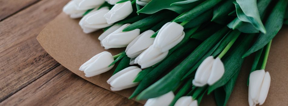A bouquet of white tulips on a brown paper wrap, set on a wooden surface.