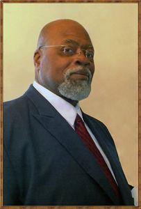 Man in suit and tie, glasses, and salt-and-pepper beard, looking to the side.