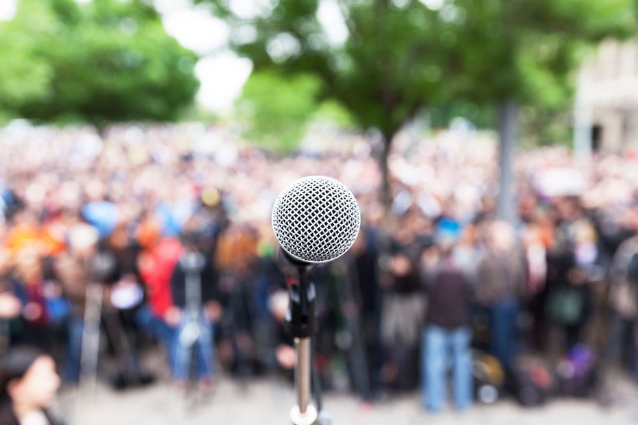 Microphone on a stand with a blurred crowd gathered outdoors in the background