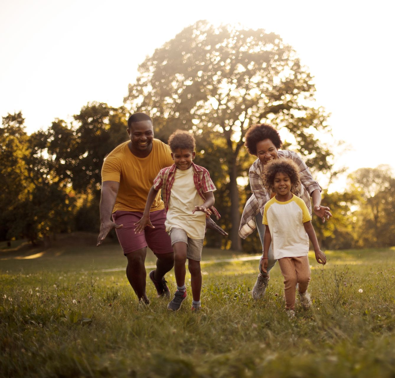 Family of four run smiling through a sunlit grassy field at sunset.