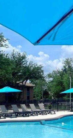Apartment pool with turquoise umbrellas beside brick buildings on a sunny day
