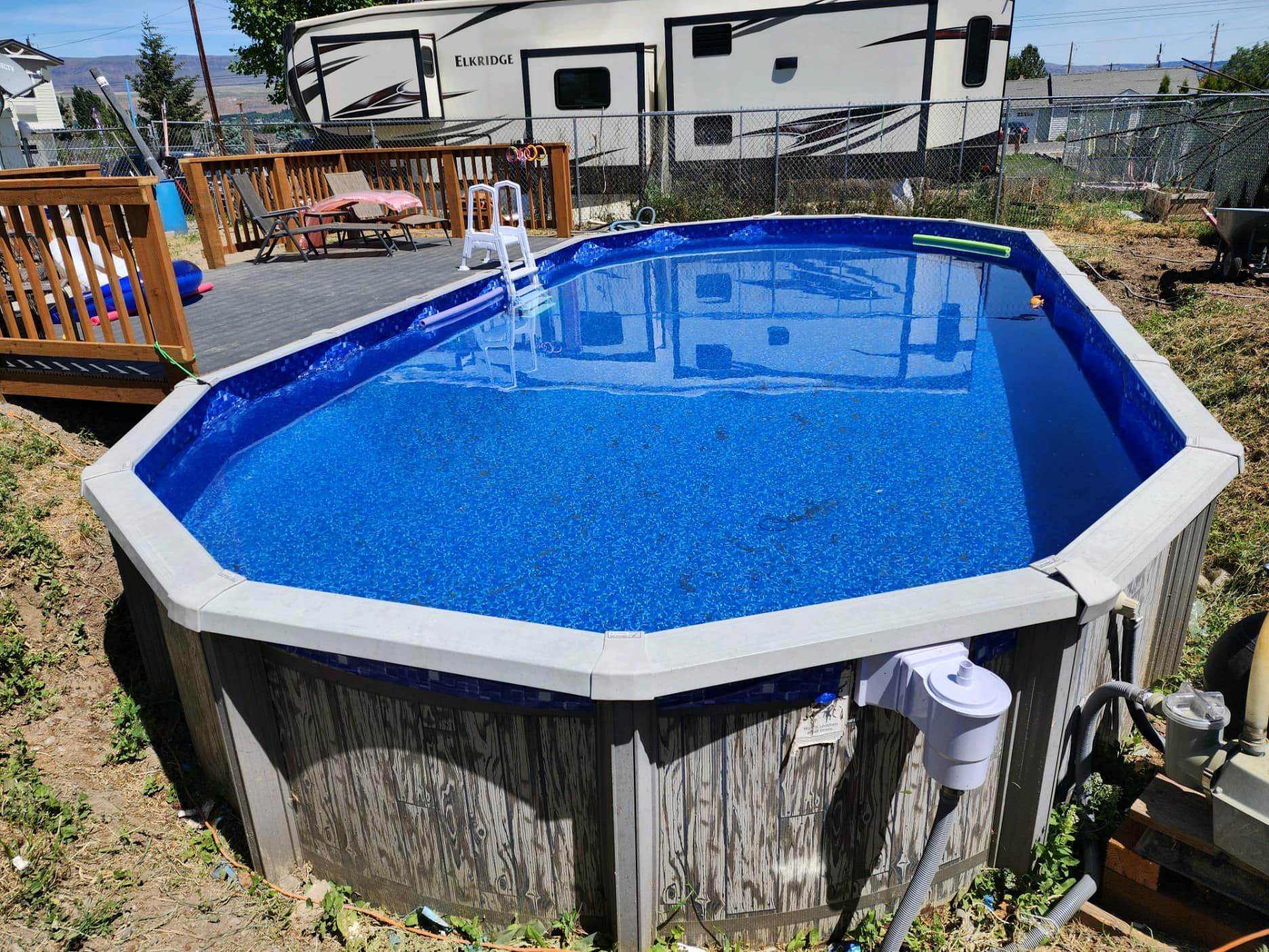 Above-ground pool with blue water, a wooden deck, and an RV in the background.