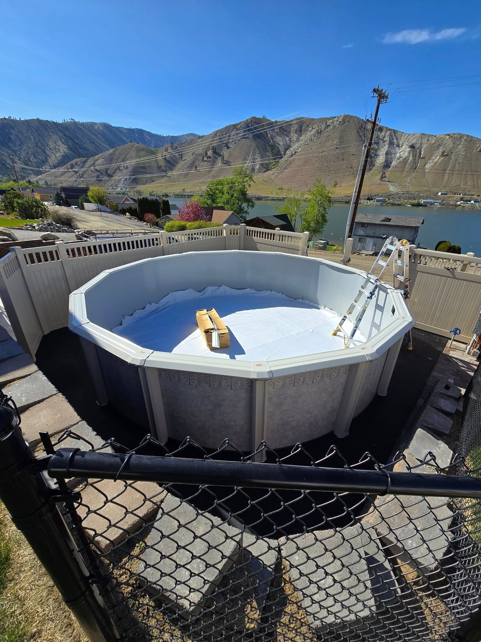 Above-ground pool being assembled with a scenic mountain and lake backdrop.