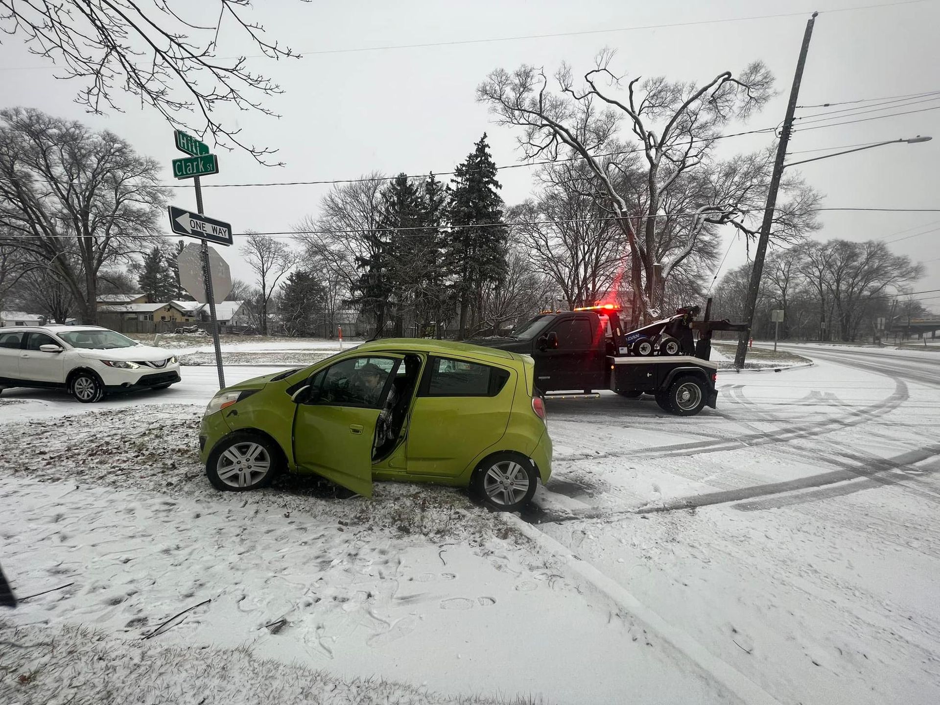 A yellow car is being towed by a tow truck in the snow.