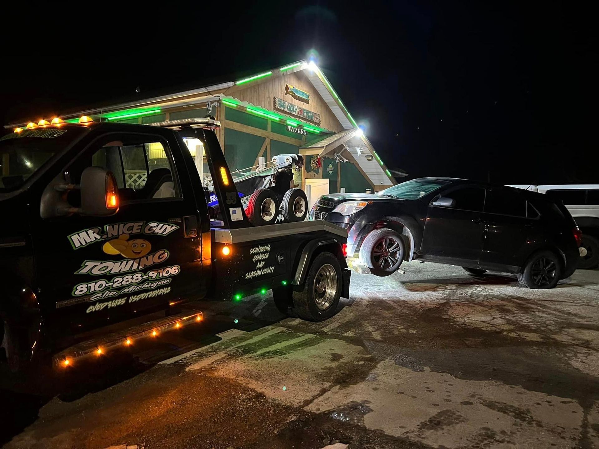 A tow truck is towing a car in front of a building at night.