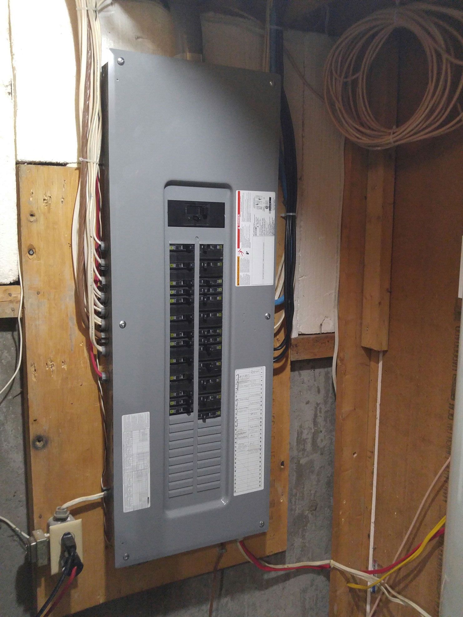 Un panneau électrique est accroché à un mur en bois dans un sous-sol.
