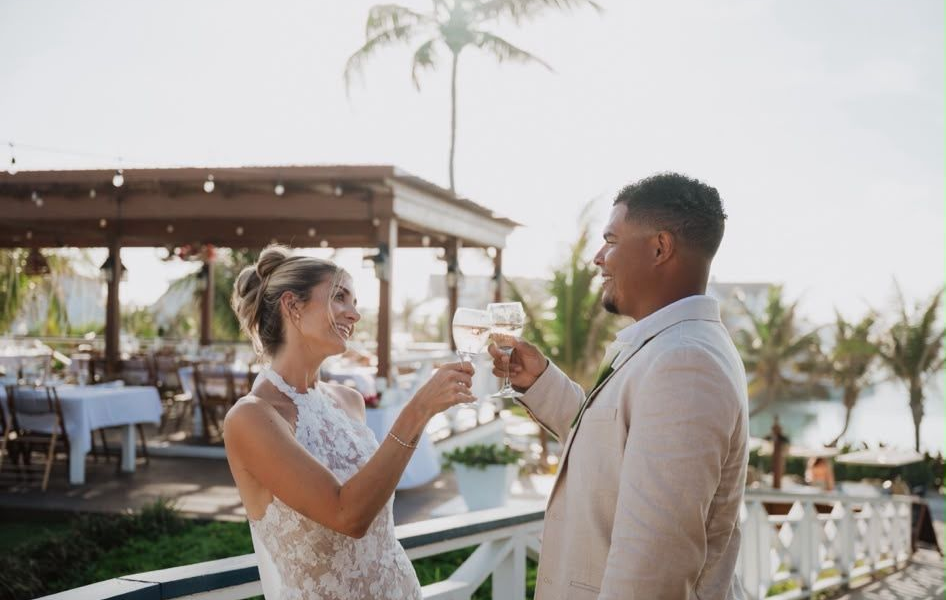 Two people toasting drinks outdoors at a waterfront wedding reception
