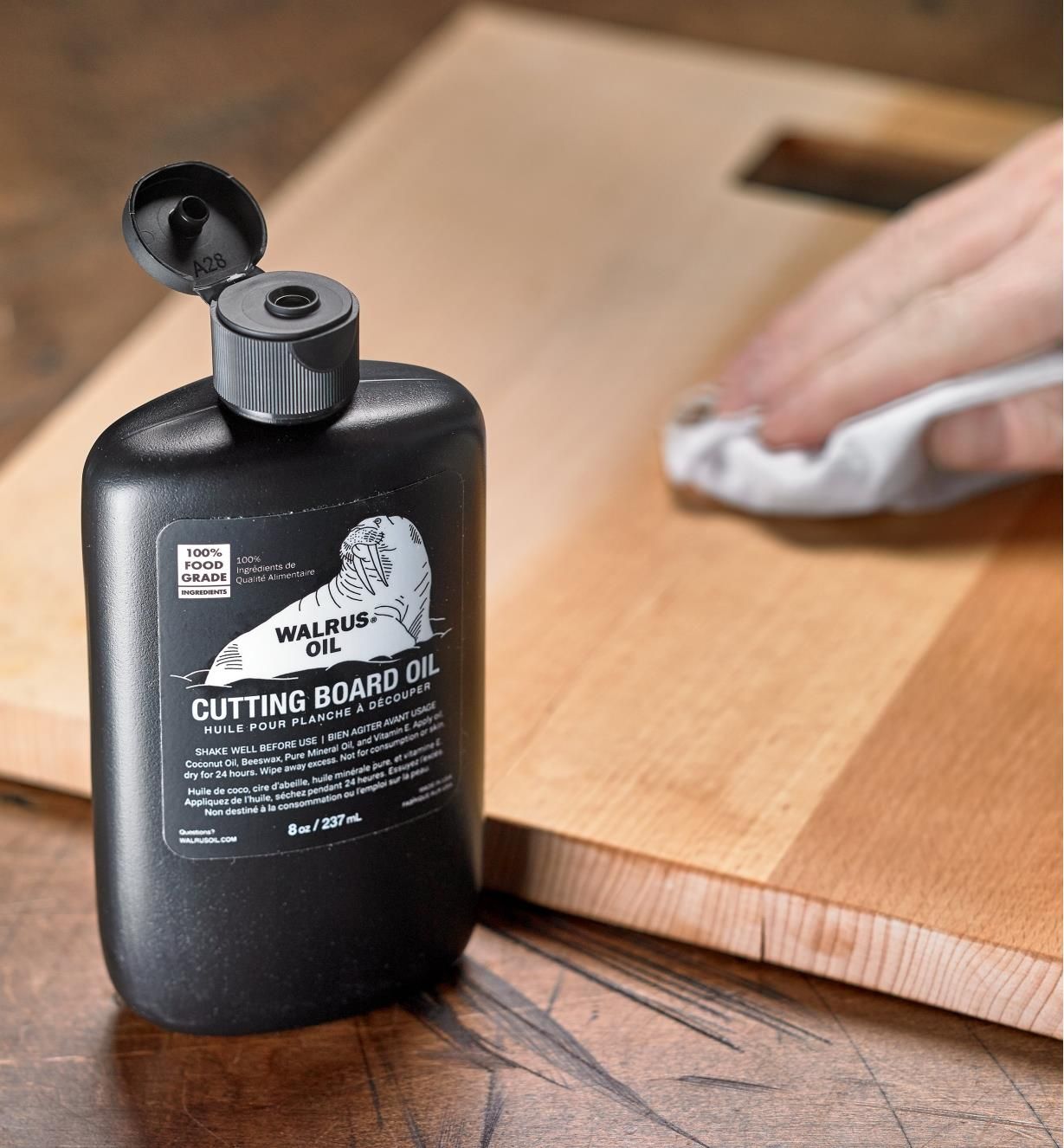 A person is cleaning a cutting board with a bottle of cutting board oil