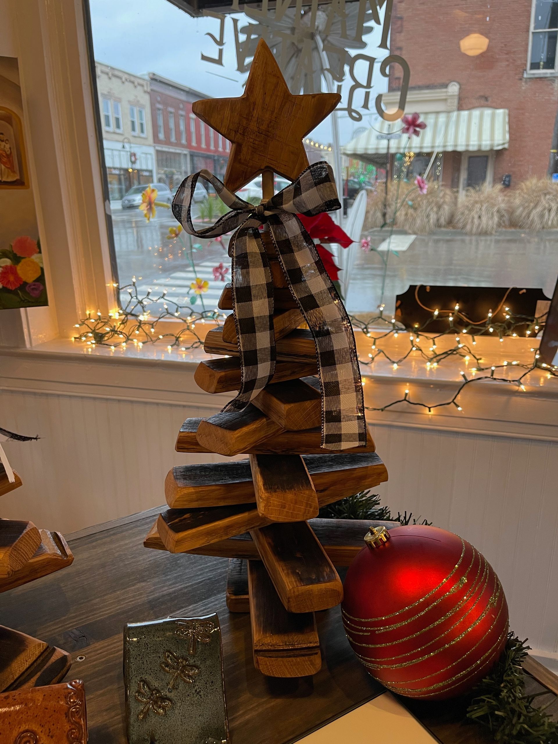 A wooden christmas tree with a star on top is sitting on a table next to a red ball.