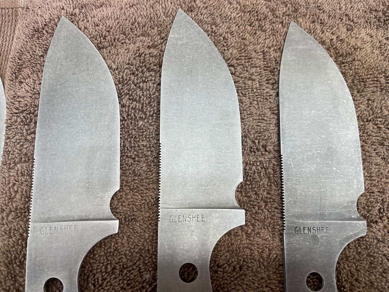 Four knives are lined up in a row on a brown cloth