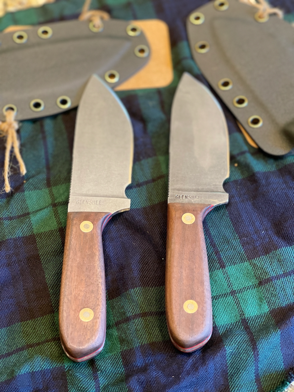 Two knives with wooden handles are on a plaid cloth