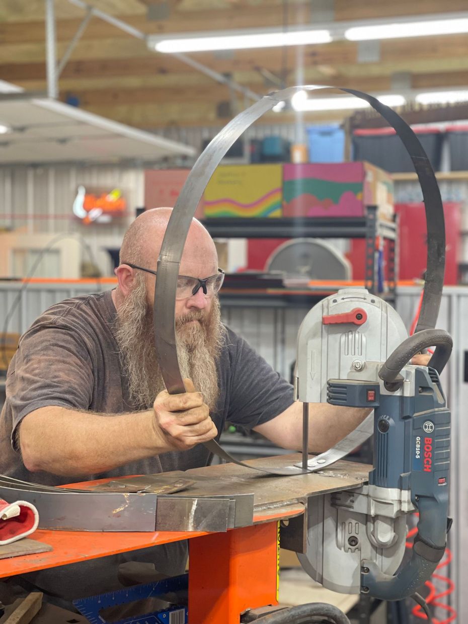 A man with a beard is working on a piece of metal in a workshop.