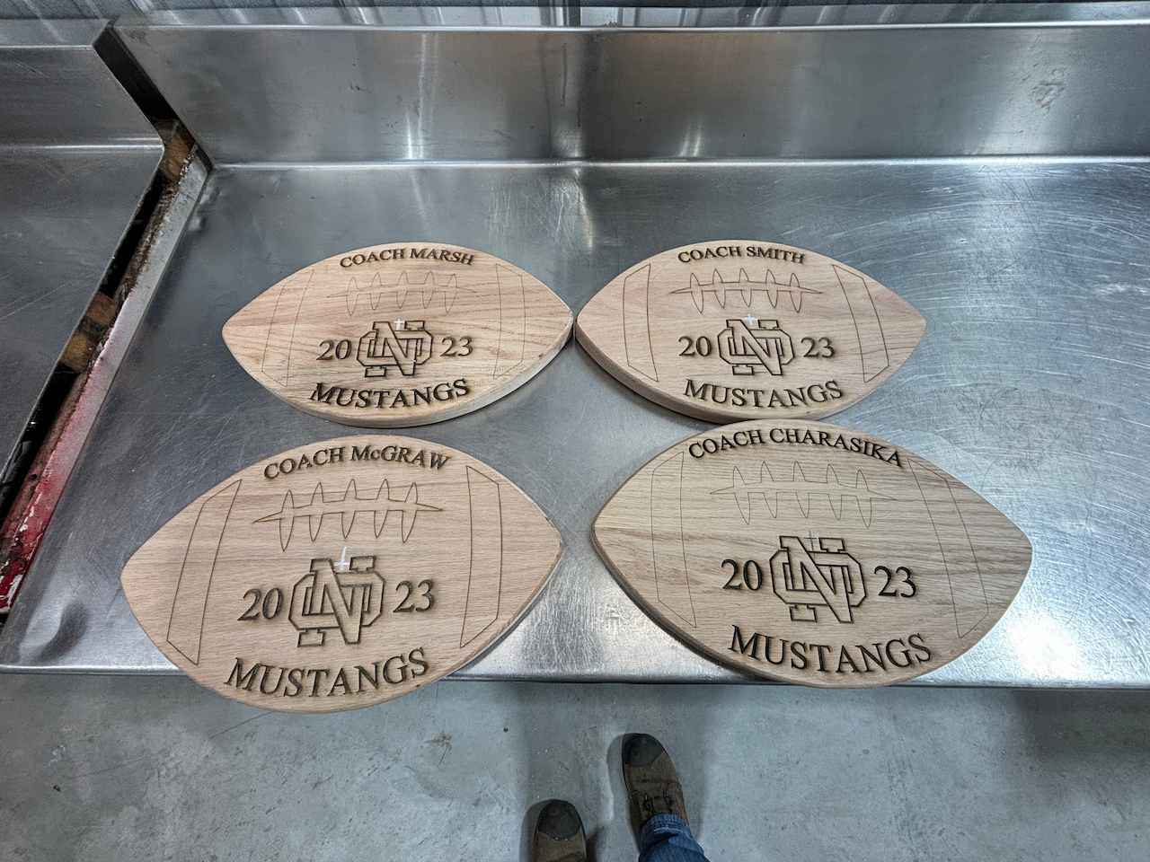 Four wooden football shaped coasters are sitting on a stainless steel counter.