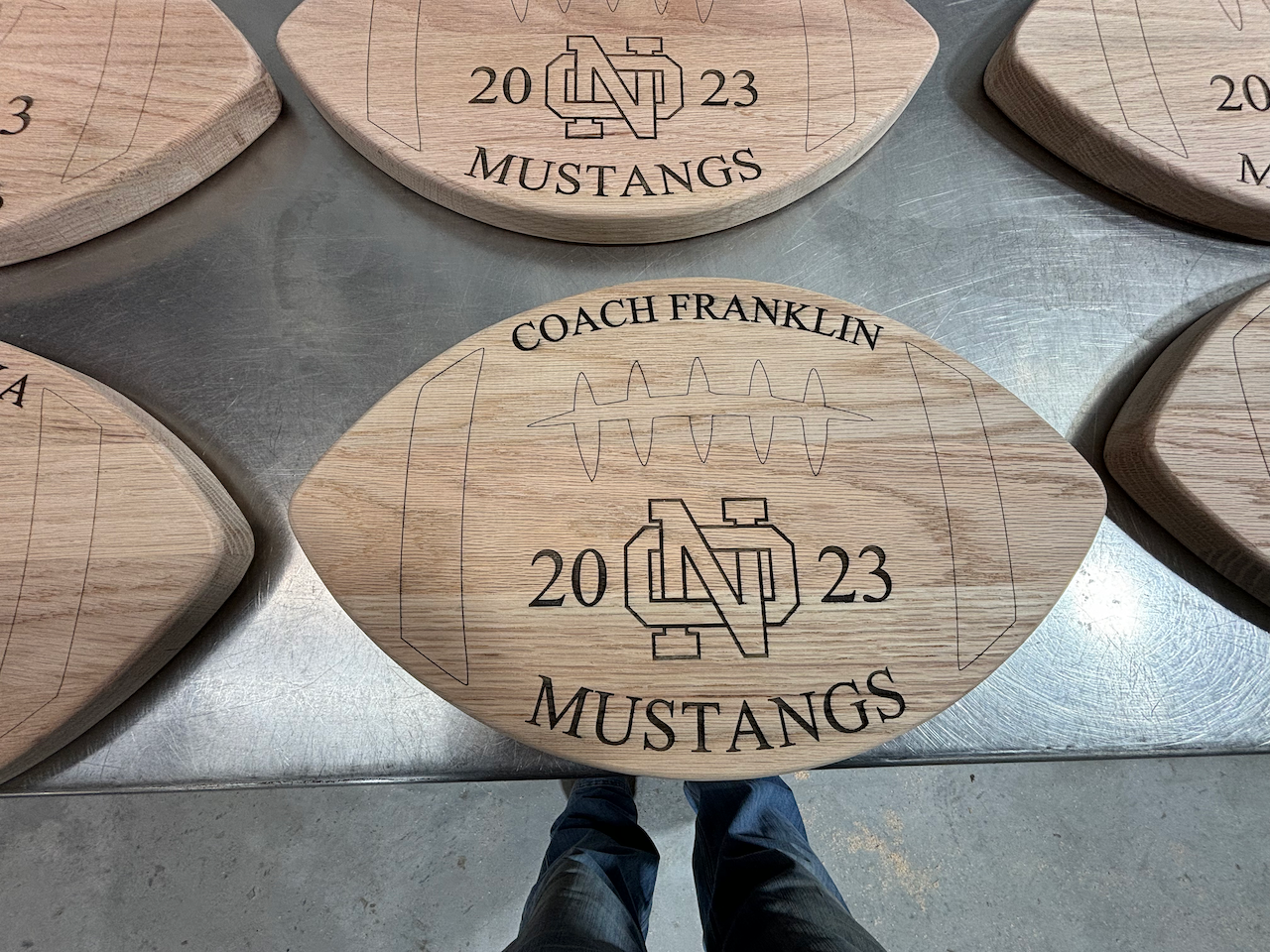 A person is standing next to a wooden football with the word mustangs on it.
