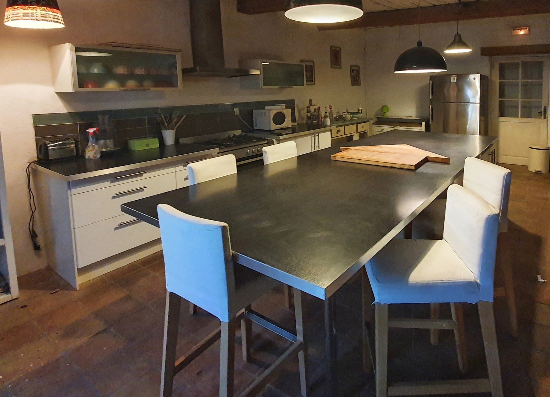 Cuisine moderne avec un grand îlot central foncé, des tabourets blancs et un éclairage suspendu chaleureux.
