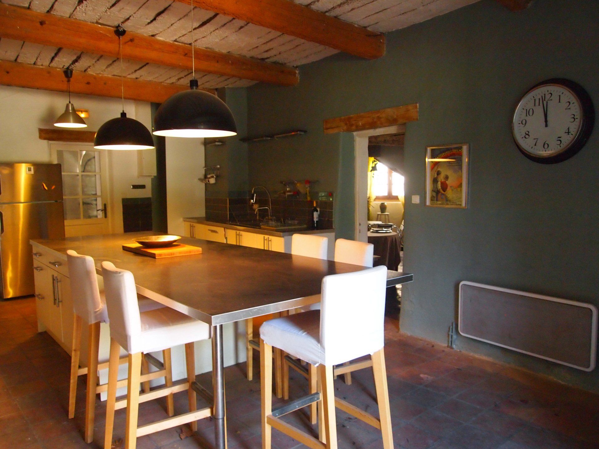Salle à manger moderne avec une longue table en bois, des chaises blanches, des suspensions lumineuses et une horloge murale.