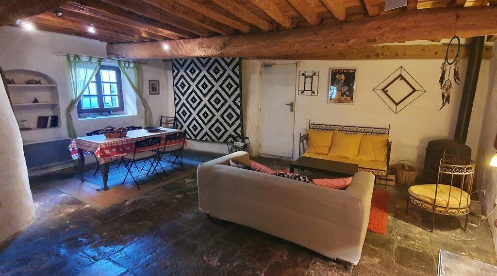 Salon rustique et chaleureux avec poutres apparentes, tapis à motifs, canapé, table et éclairage d'ambiance doux.
