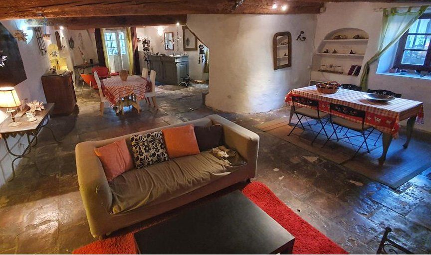 Salon rustique et chaleureux avec canapé, table en bois et éclairage tamisé ; coin repas visible au fond.