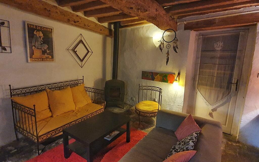 Salon rustique et chaleureux avec canapé jaune, fauteuil foncé, table basse, cheminée et plafond à poutres apparentes.