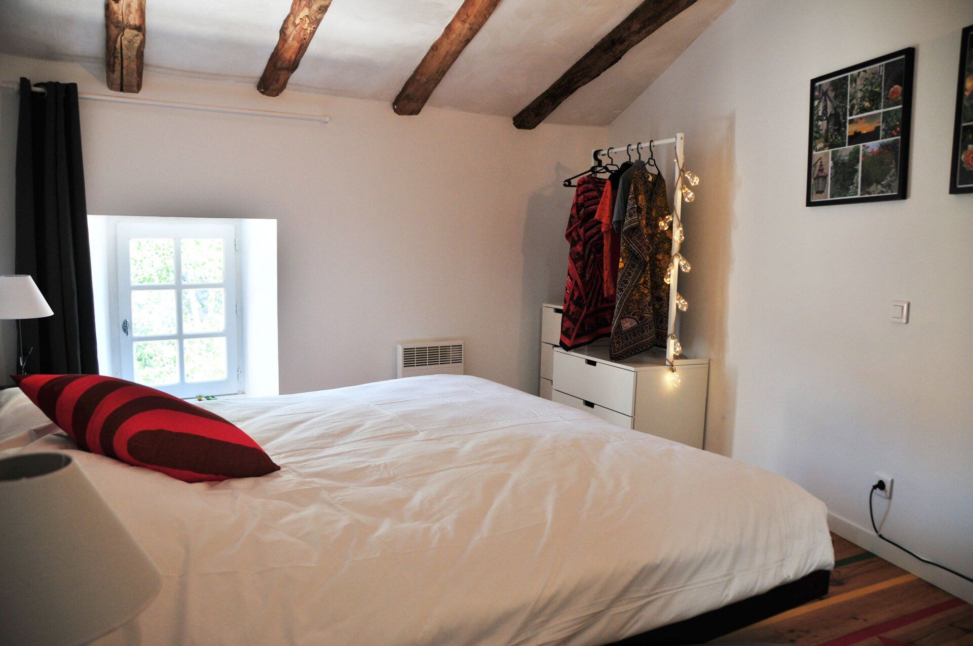 Chambre lumineuse avec couvre-lit blanc, poutres apparentes au plafond, fenêtre, décorations murales et éclairage.