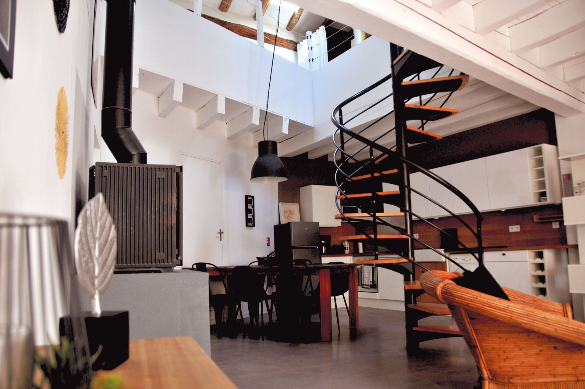 Intérieur de loft moderne avec escalier en colimaçon, murs blancs, meubles foncés et fauteuil en osier