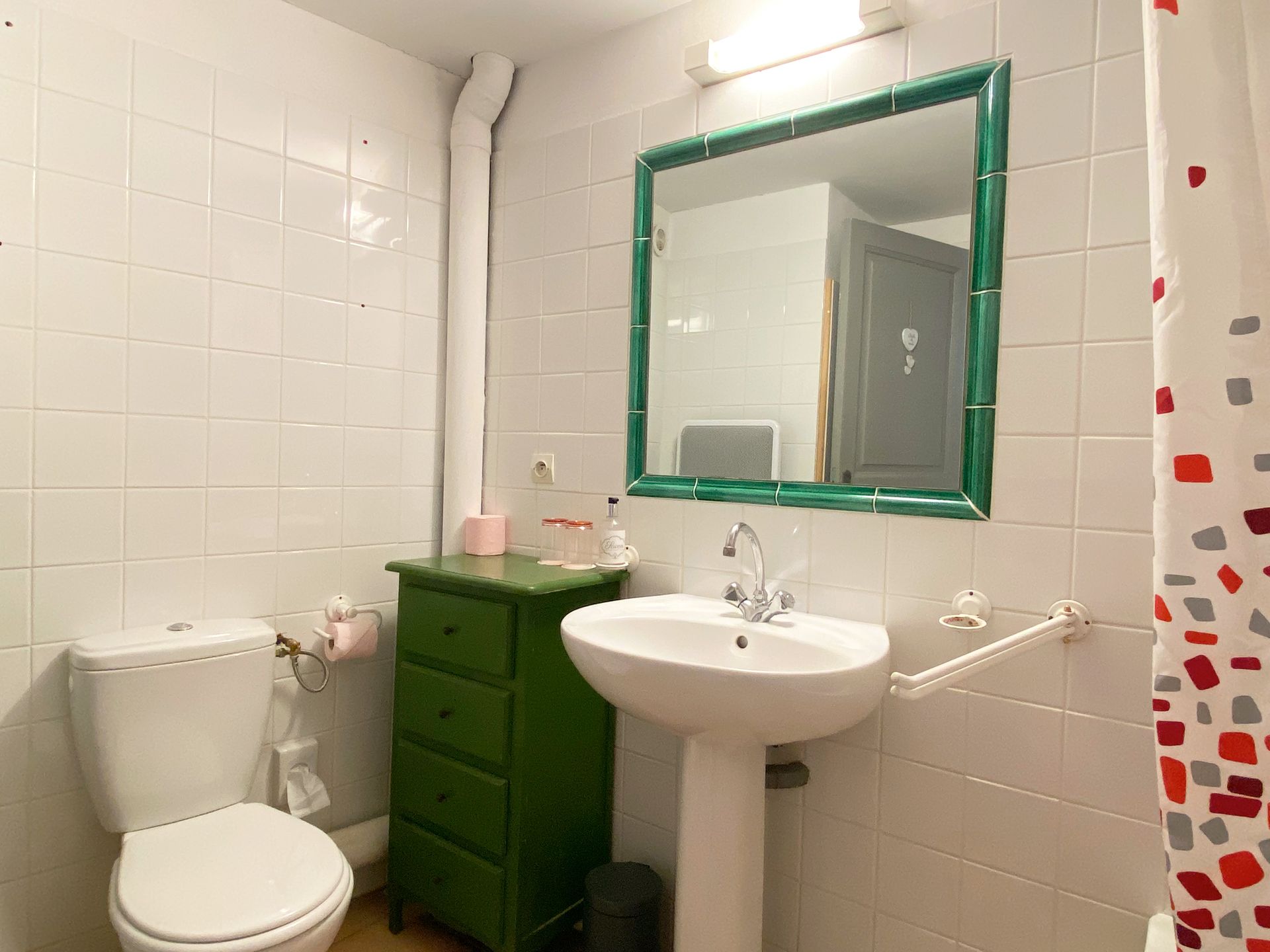 Petite salle de bains blanche avec lavabo sur pied, toilettes, armoire verte et miroir au-dessus du lavabo.
