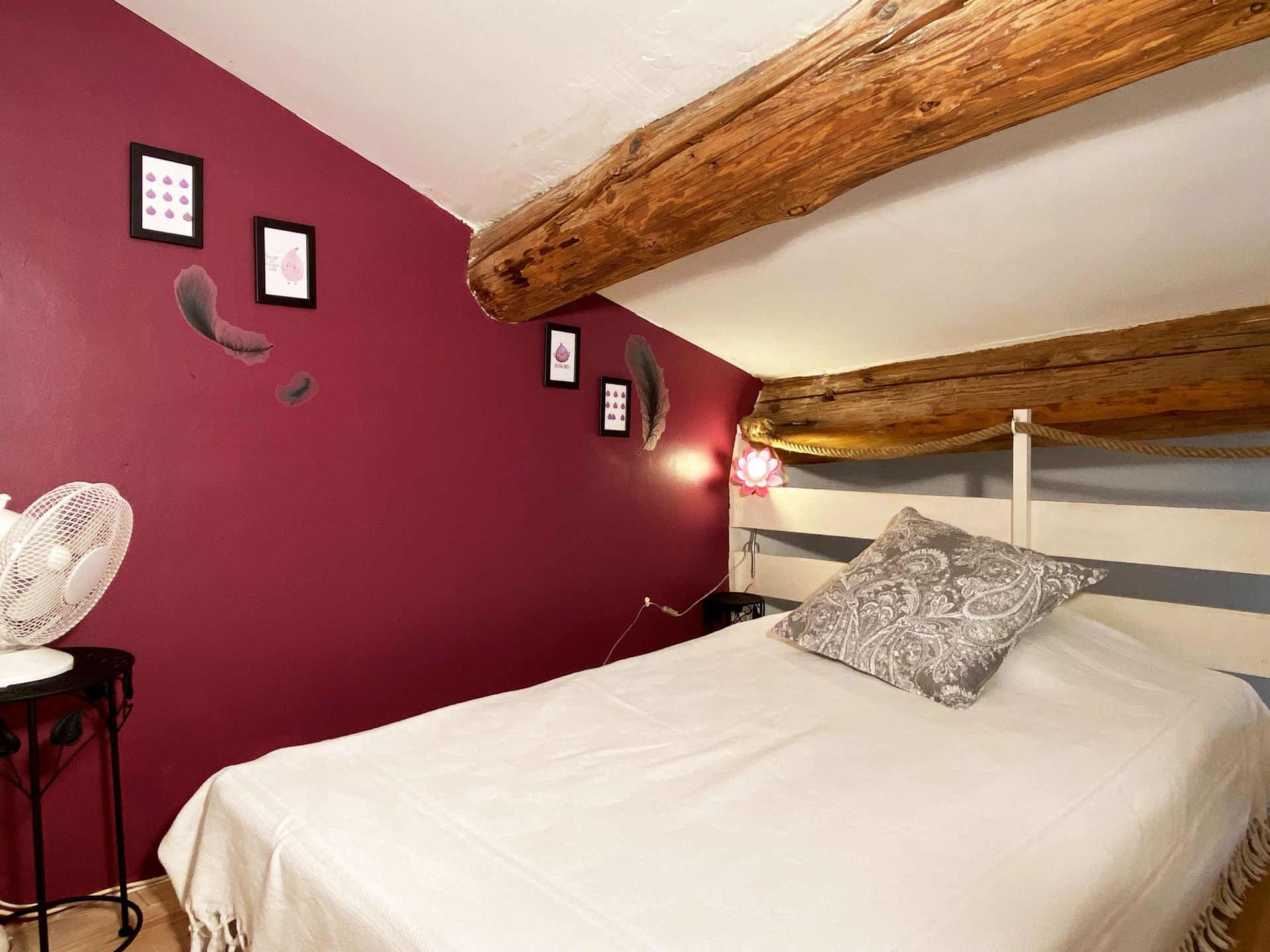 Chambre mansardée confortable avec poutres apparentes, mur magenta et lit avec draps blancs et oreiller à motifs