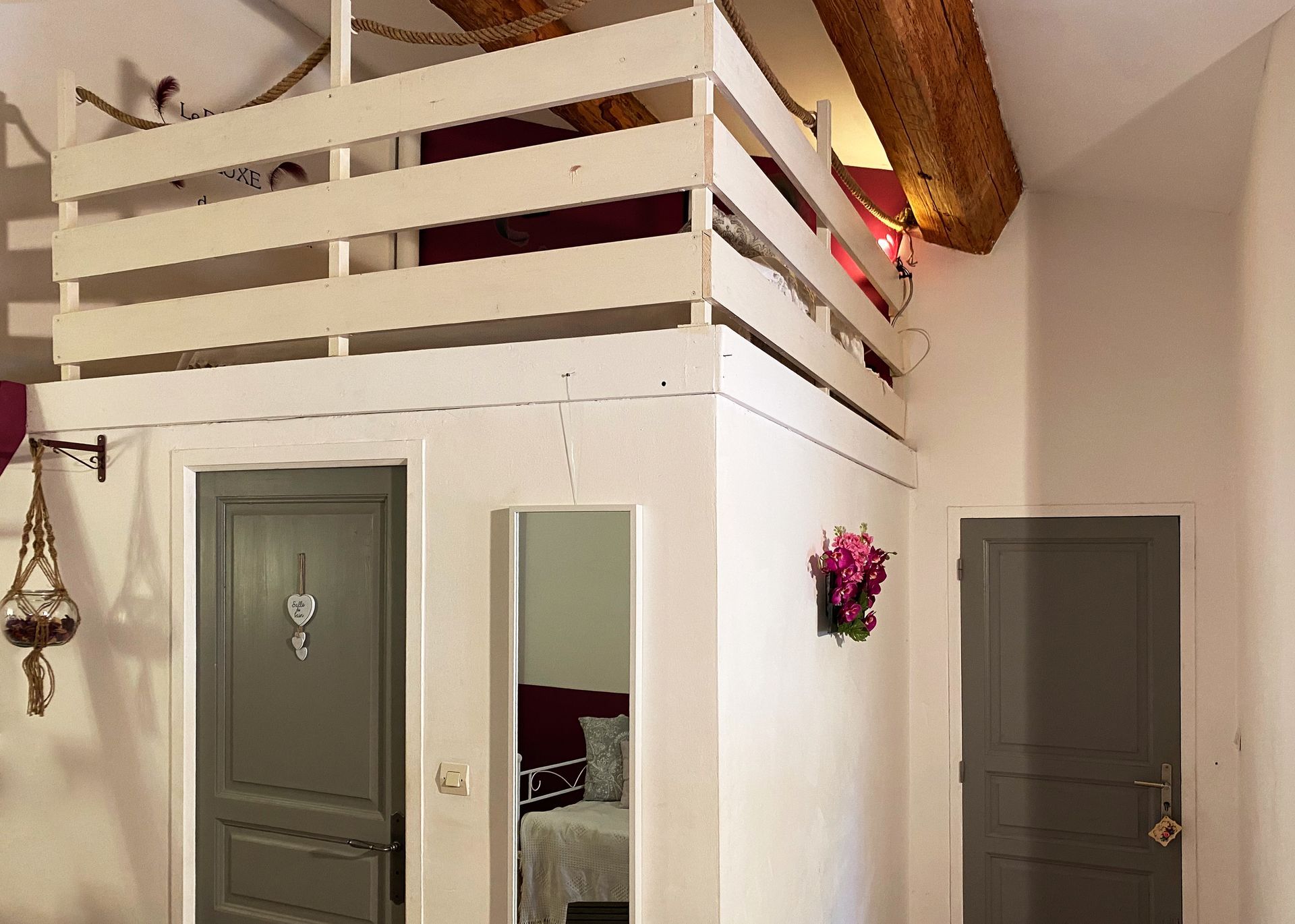 Chambre de style loft avec murs blancs, portes grises et une petite balustrade de balcon au-dessus