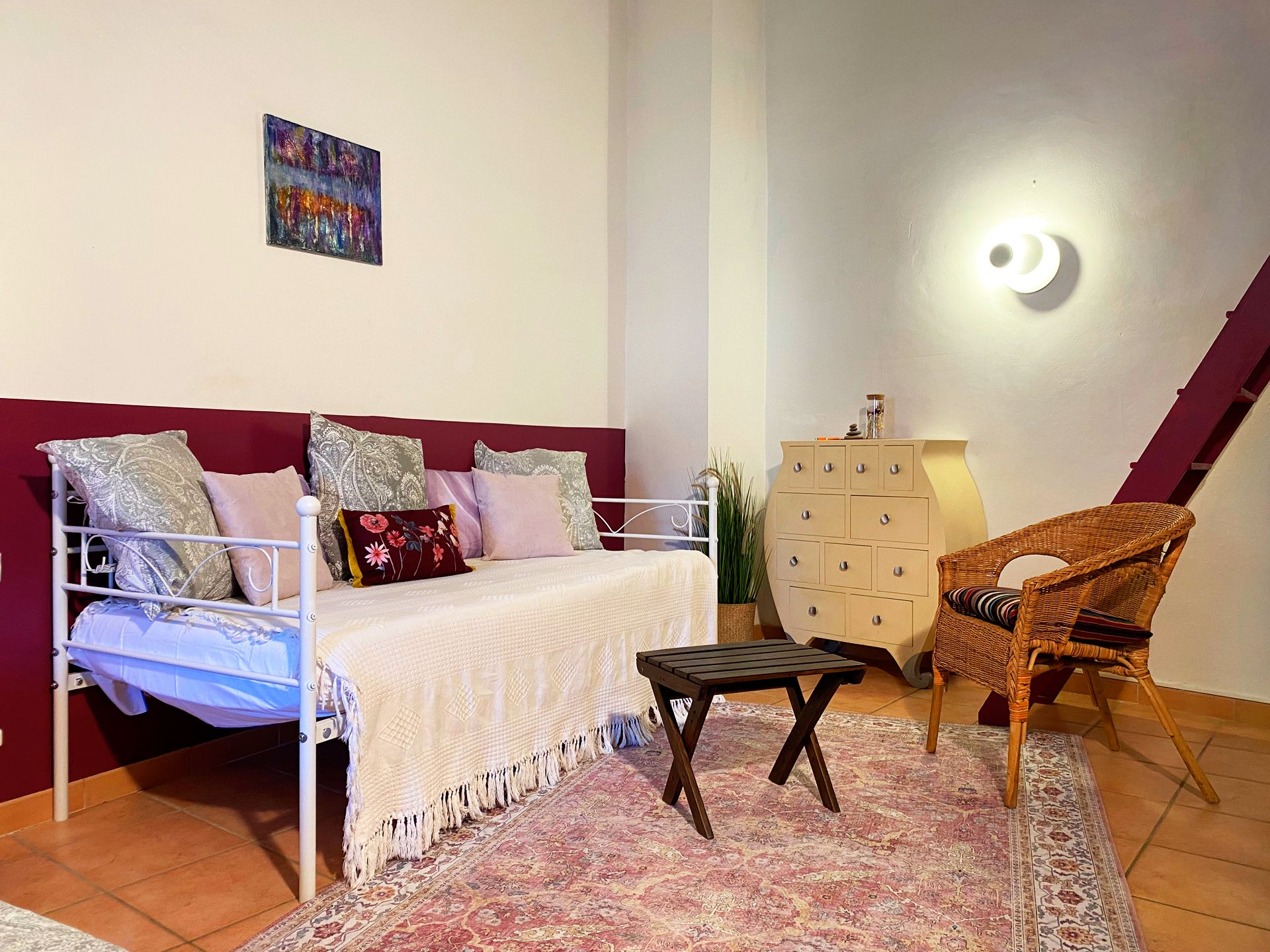 Chambre confortable avec un lit, une chaise, une petite table, une commode et des décorations murales dans des tons rose pâle et blanc.
