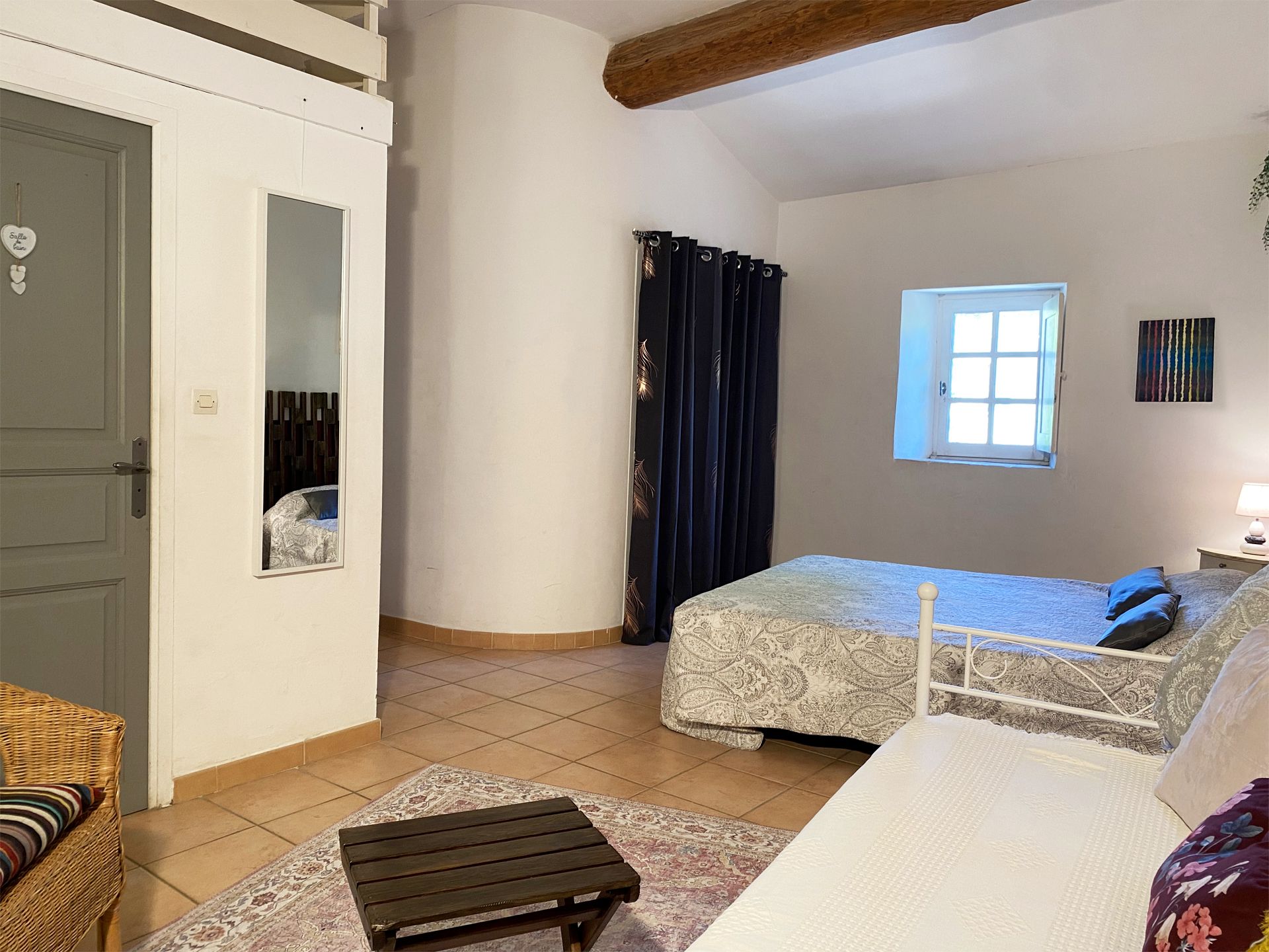 Petite chambre avec un lit, une armoire, une fenêtre et un tapis à motifs dans des tons neutres et doux.
