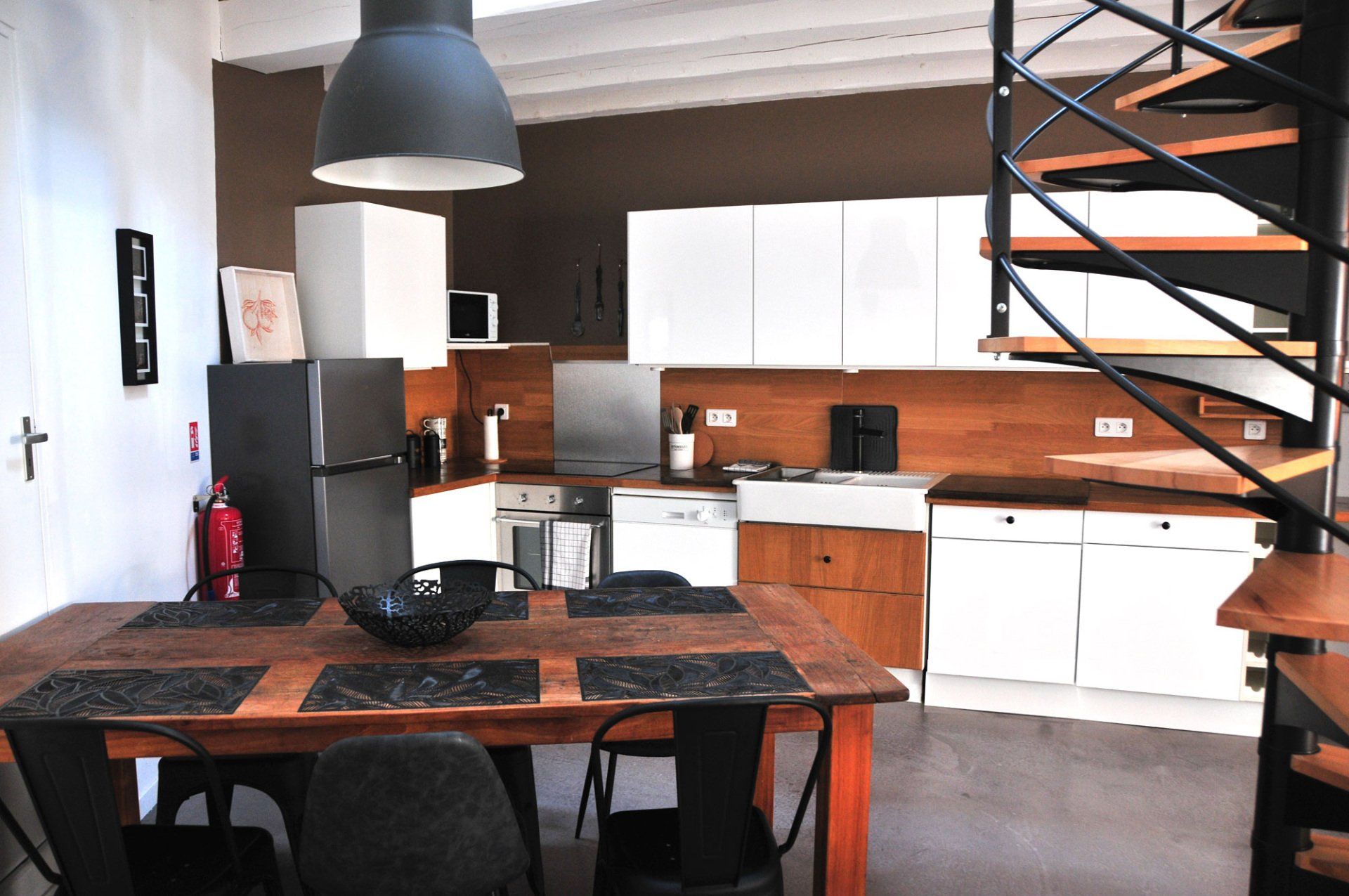 Cuisine et salle à manger modernes avec placards blancs, table noire et escalier en colimaçon
