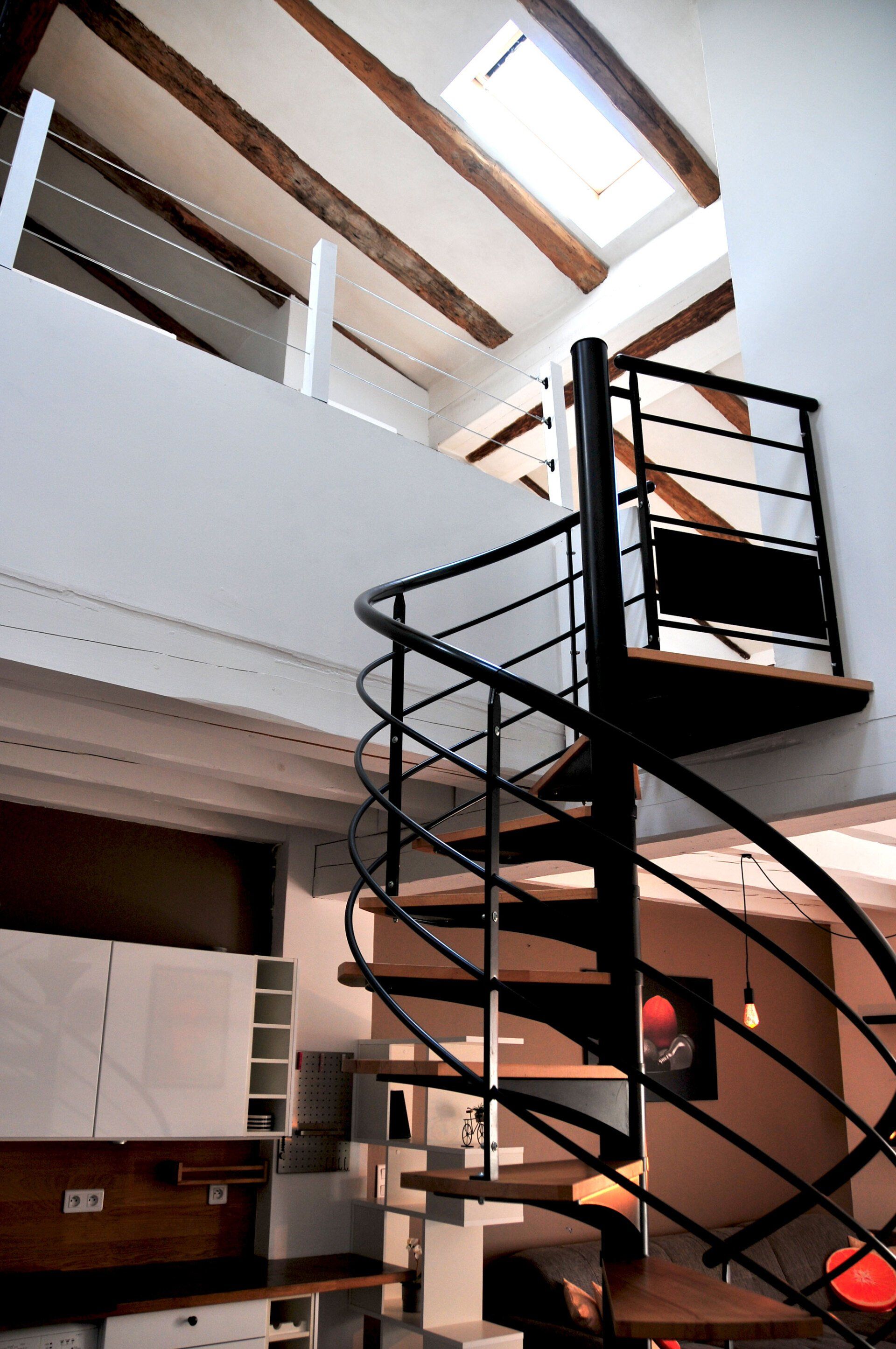 Loft intérieur avec un escalier en colimaçon noir et des murs blancs sous des fenêtres de toit