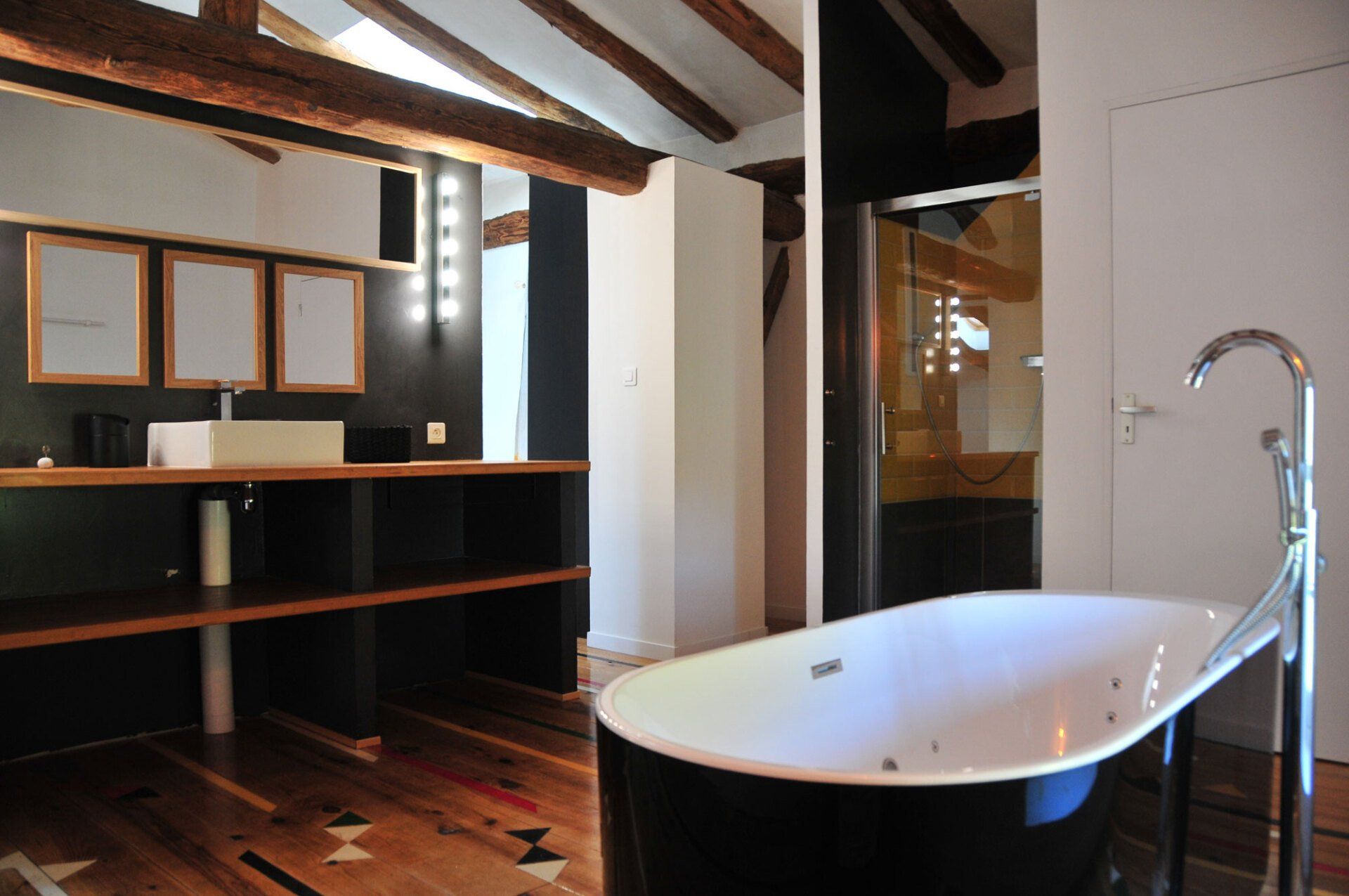 Salle de bains moderne avec baignoire îlot, plafond à poutres apparentes et meuble-lavabo.