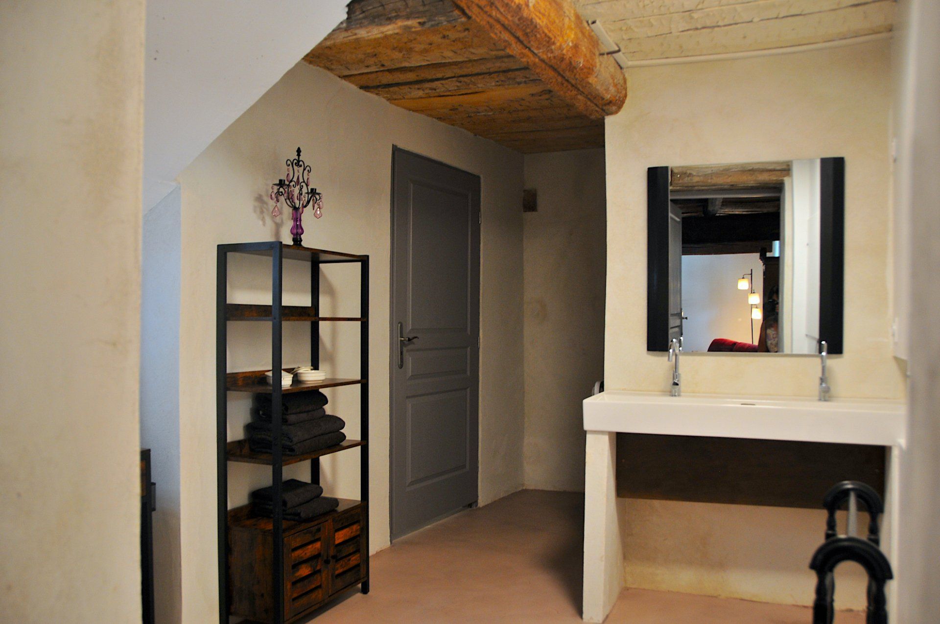 Chambre confortable avec plafond en bois incliné, étagère, porte fermée et coiffeuse blanche avec miroir.