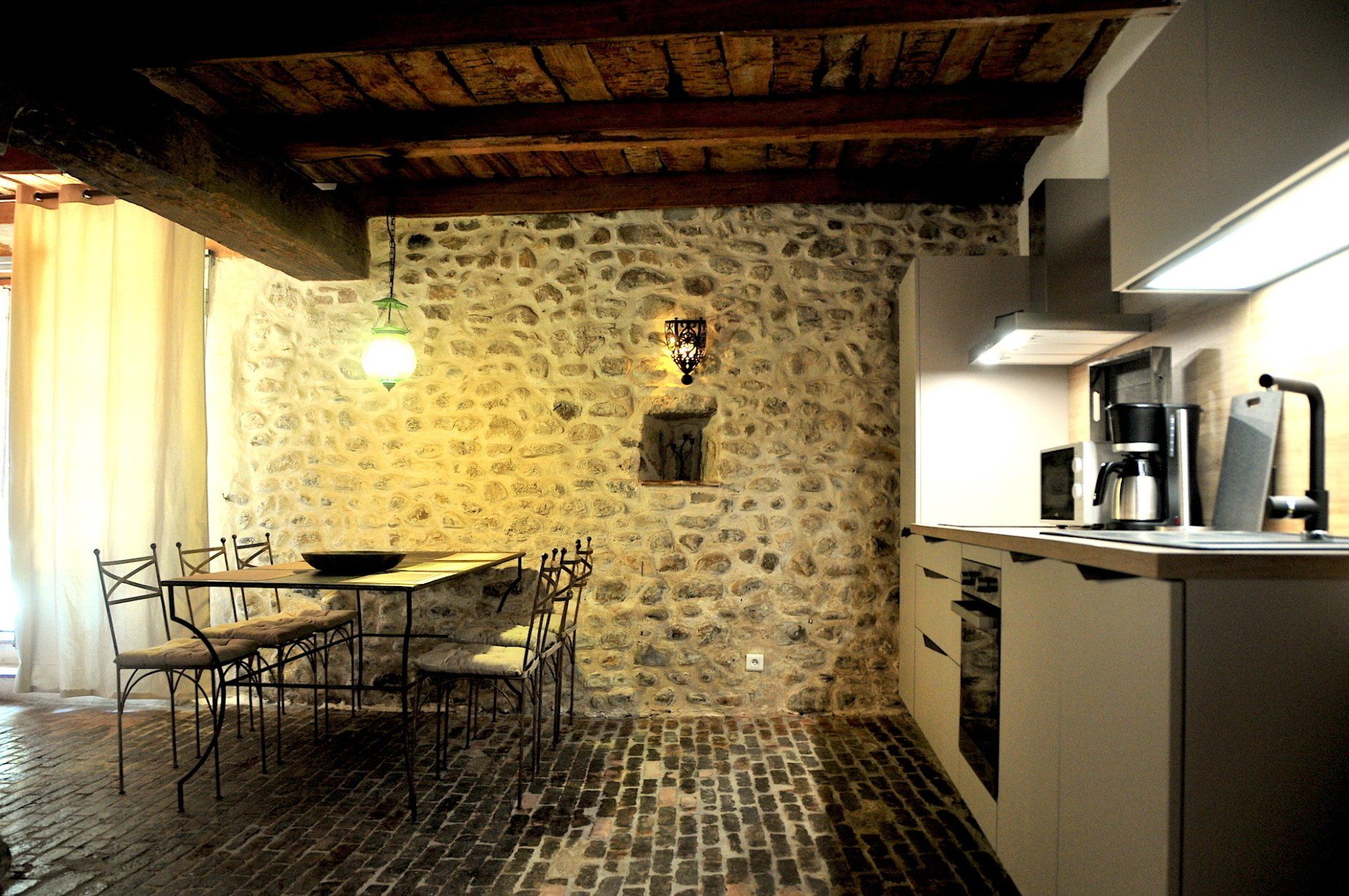 Cuisine et salle à manger rustiques et chaleureuses avec mur en pierre, poutres en bois, table et appareils électroménagers modernes