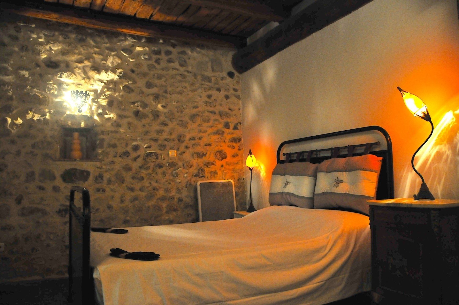 Chambre rustique et chaleureuse avec mur en pierre, plafond en bois et lampes de chevet à l'ambiance chaleureuse.