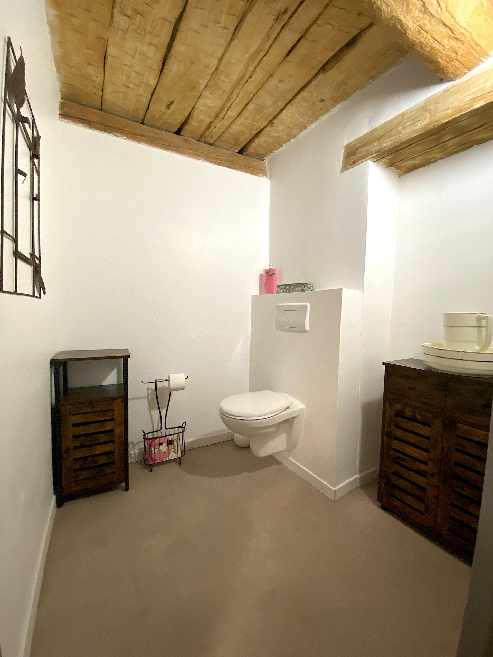 Petite salle de bains avec toilettes blanches, plafond en bois et placards de rangement en bois foncé de chaque côté.