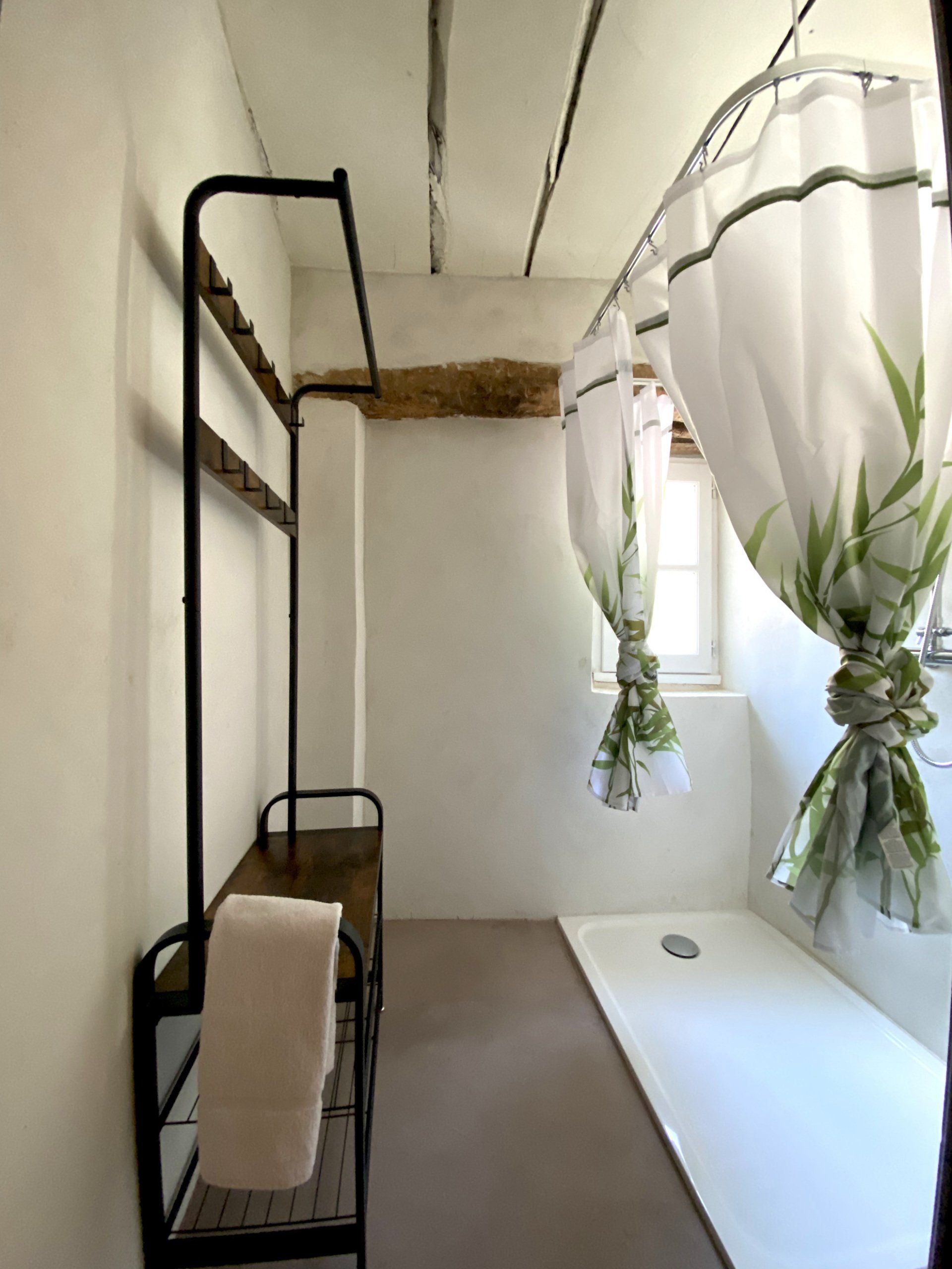 Couloir minimaliste avec rideaux blancs, plantes suspendues et un portant à vêtements en métal noir près d'une fenêtre.