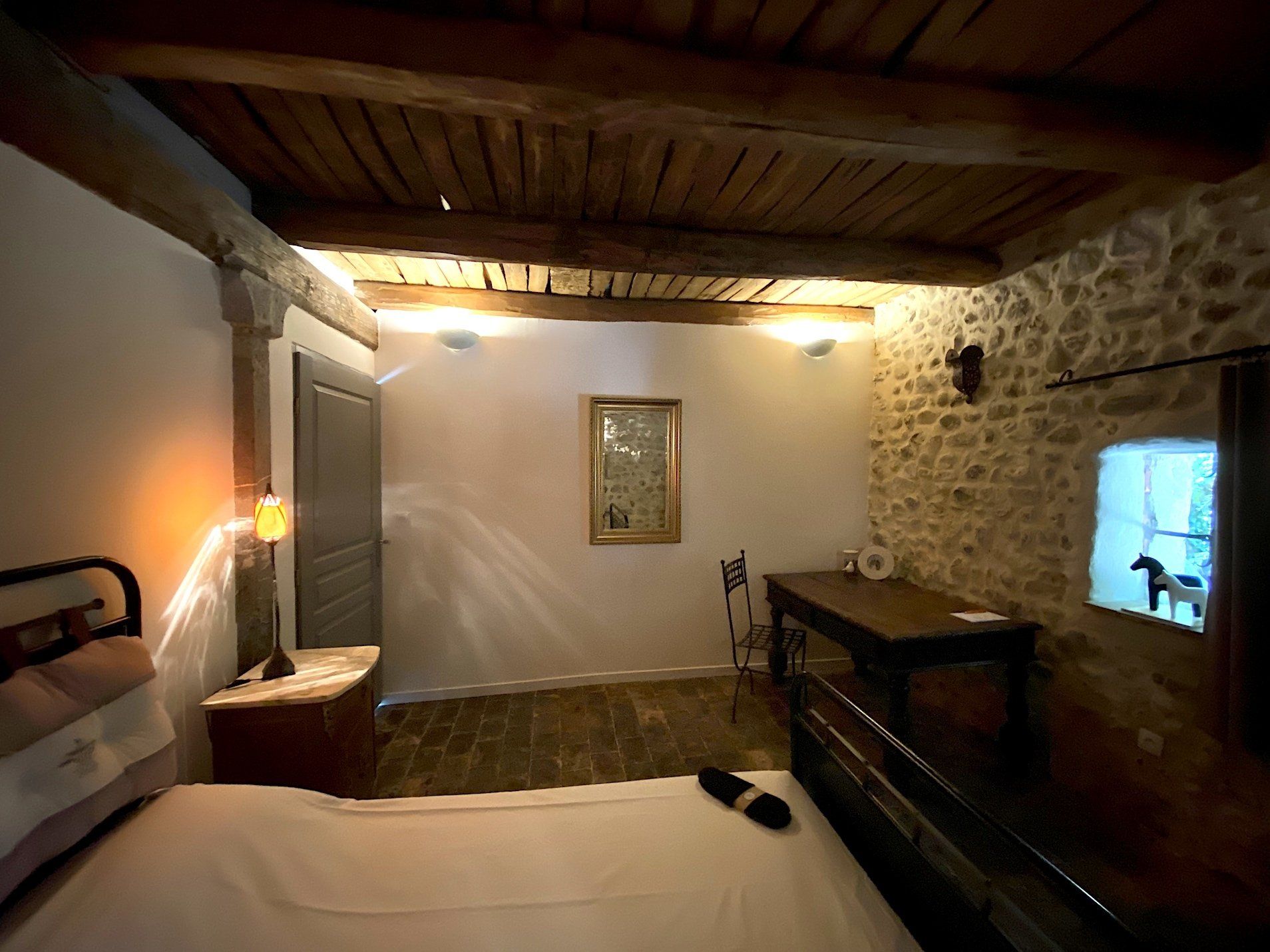 Chambre rustique avec murs en pierre, poutres en bois, un lit et des appliques murales à l'ambiance chaleureuse la nuit