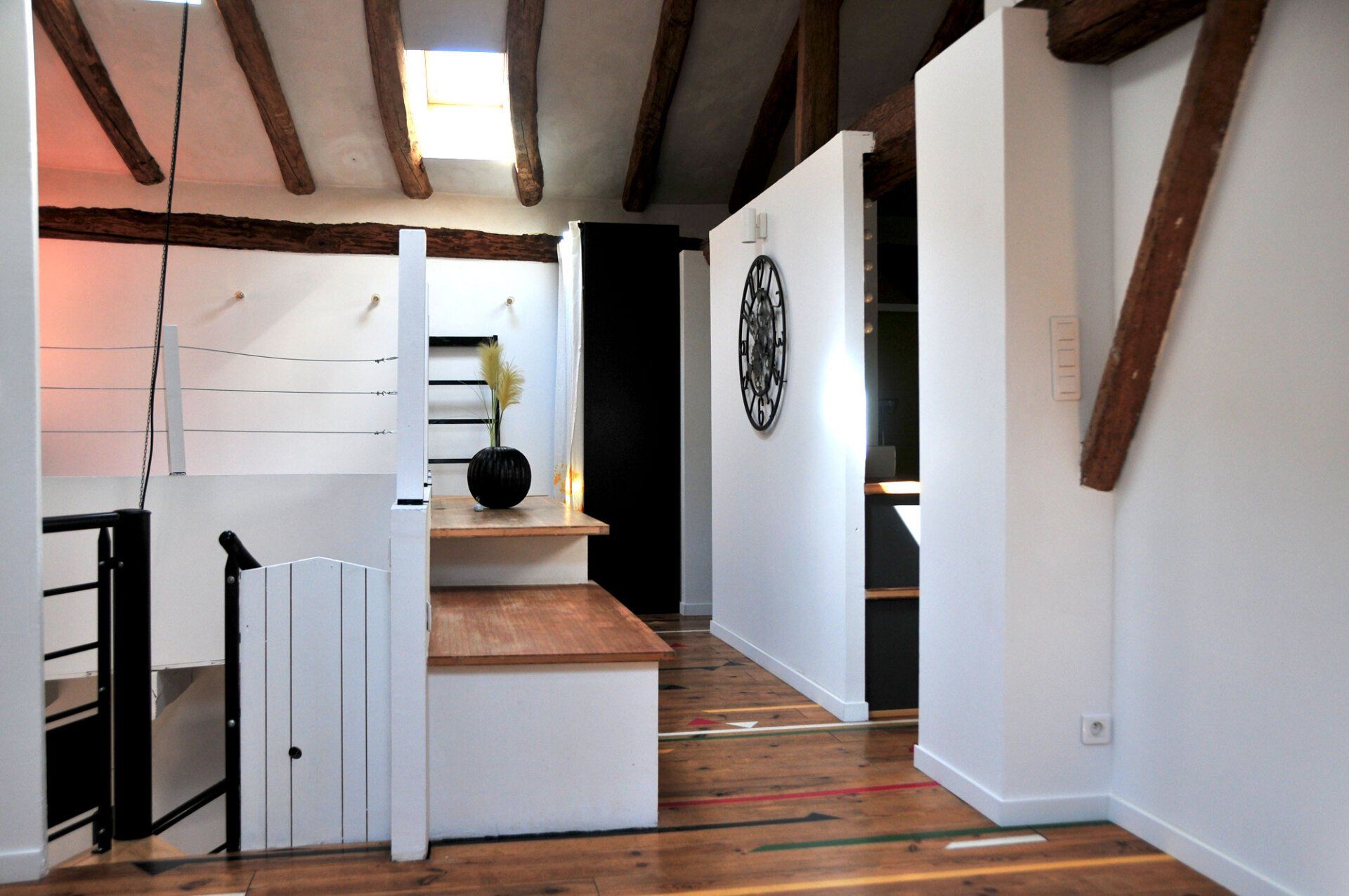 Petite cuisine moderne avec murs blancs, poutres apparentes, parquet et îlot central en bois.