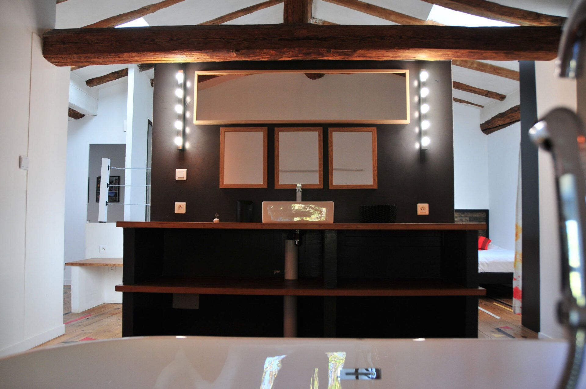 Cuisine moderne avec placards foncés, poutres apparentes et coin bar sous une lumière chaleureuse.
