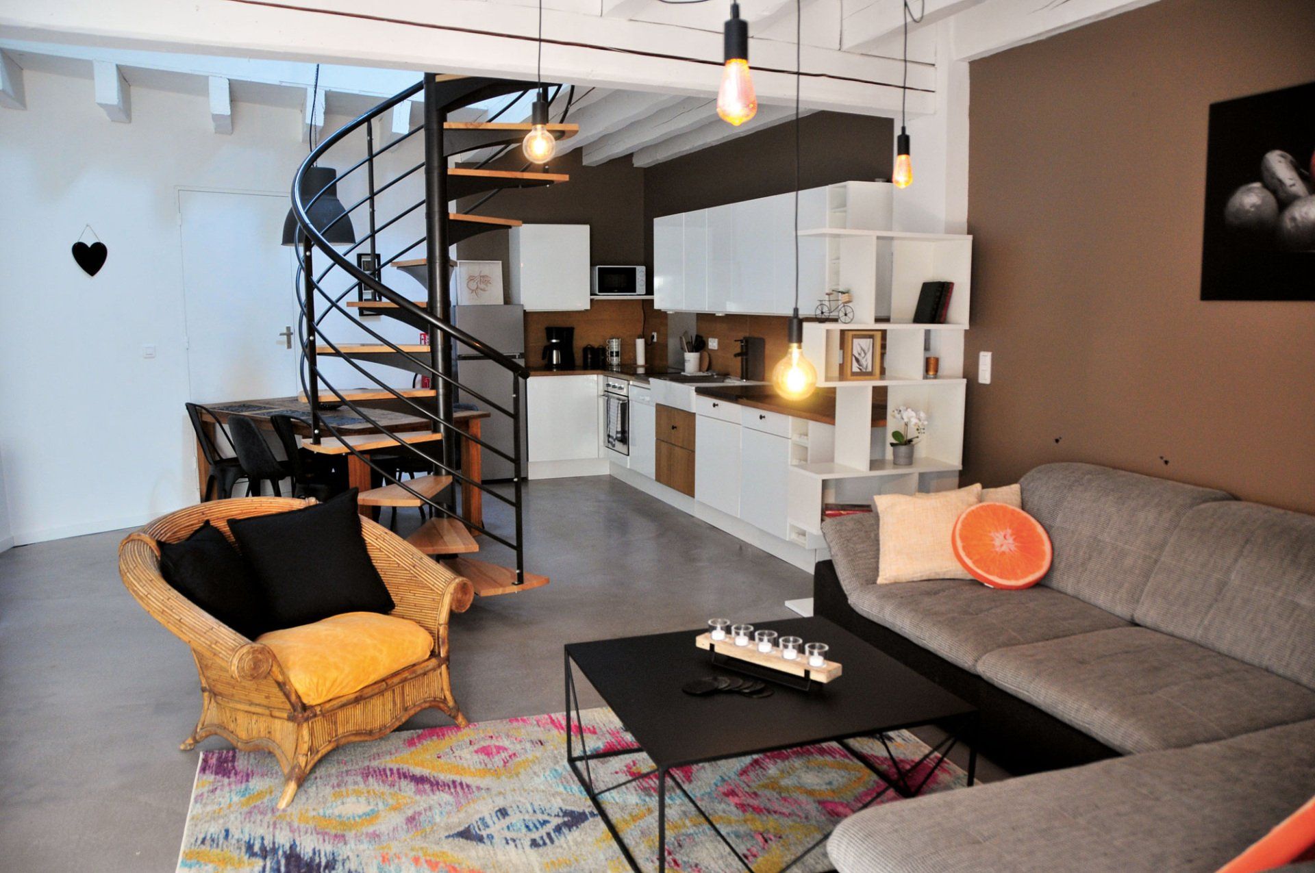 Salon loft moderne avec escalier en colimaçon, canapé gris, table basse noire et cuisine ouverte【1†source】