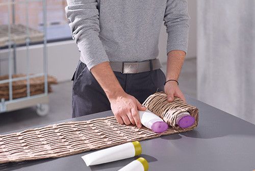 Osoba pakująca butelki z kosmetykami w opakowania z brązowego papieru.