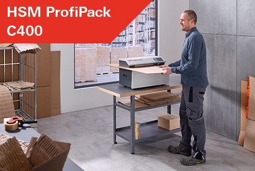 Mężczyzna używa HSM ProfiPack C400 do obróbki tektury. Maszyna stoi na stole warsztatowym. Ustawienie w magazynie.
