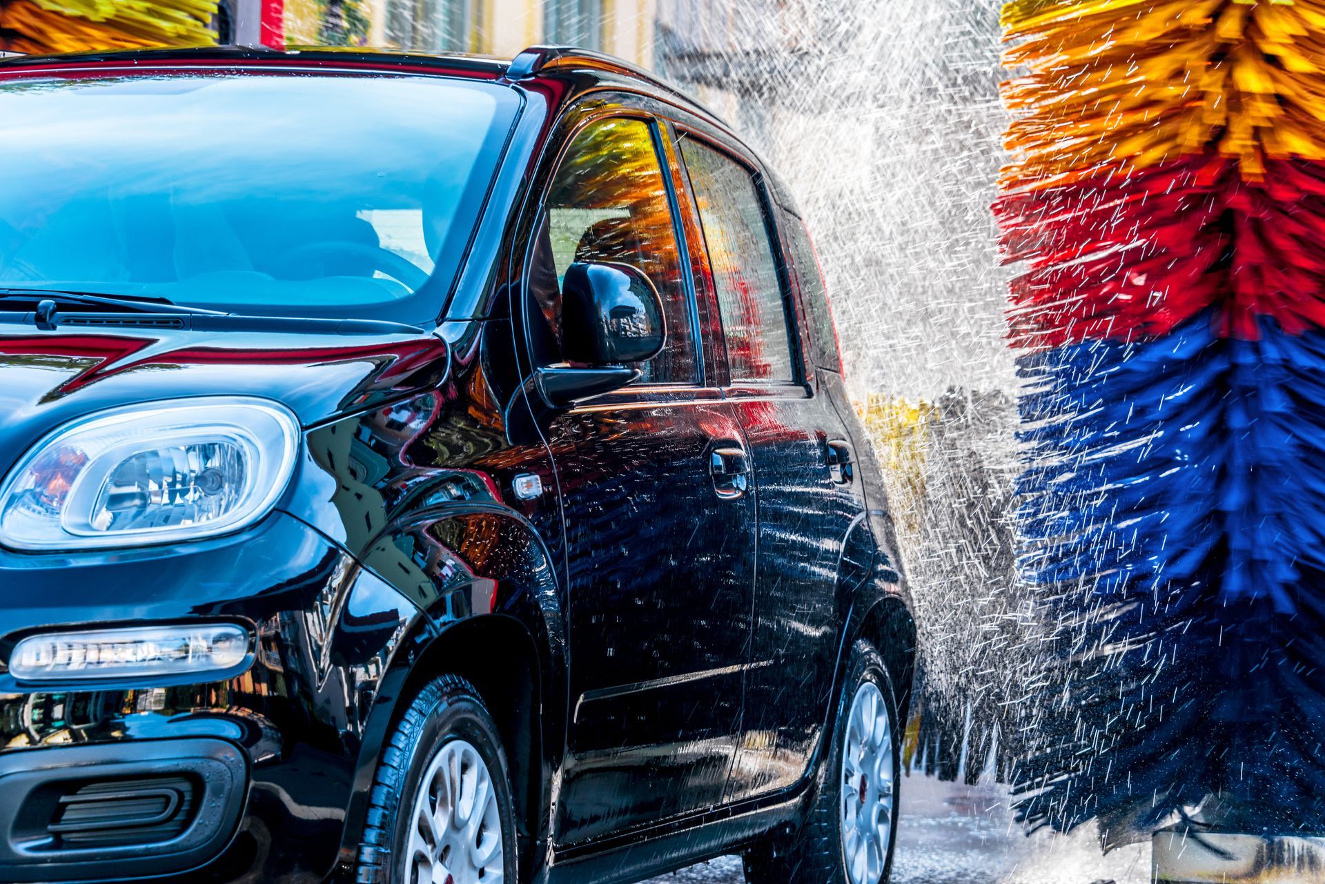 Black car moving through an automatic car wash with colorful brushes and spray.